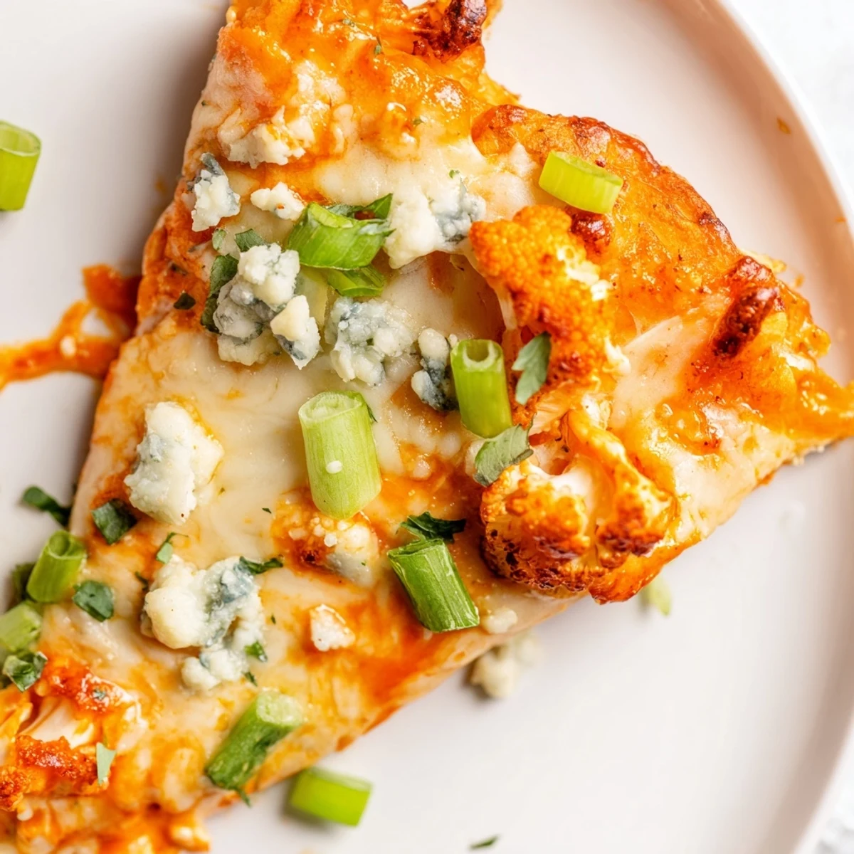 Golden-brown Buffalo Cauliflower Pizza with melted mozzarella, spicy red sauce, and fresh green onions on a crispy crust.  