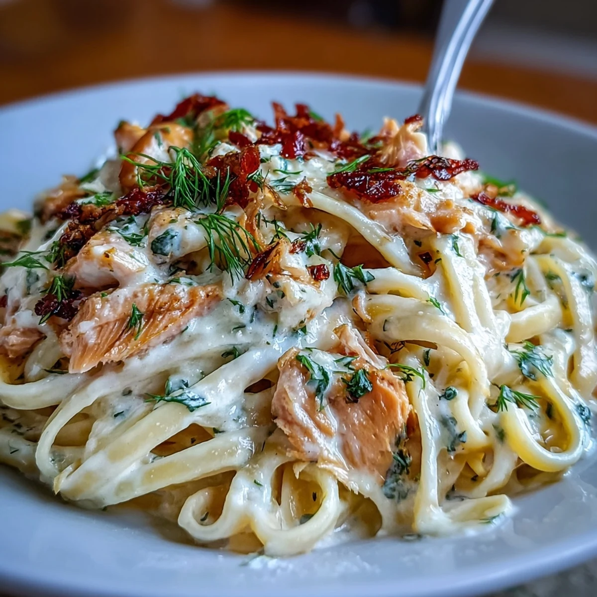 Fettuccine ribbons coated in a rich, velvety sauce studded with flaked hot-smoked salmon and Parmesan, garnished with fresh herbs on a white plate.