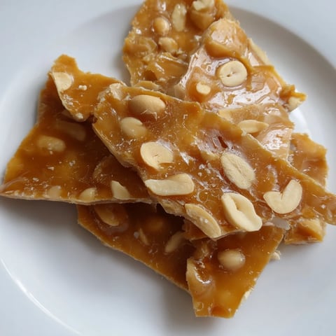 Golden peanut brittle glistening alongside its edges, a perfect homemade candy treat.