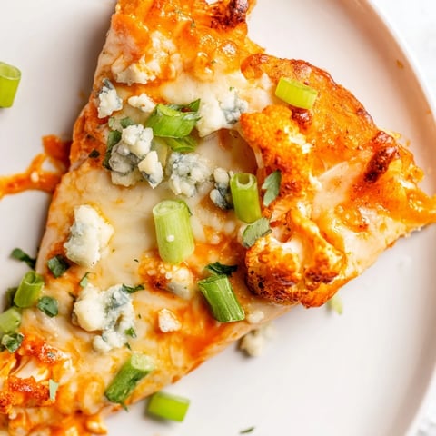 Golden-brown Buffalo Cauliflower Pizza with melted mozzarella, spicy red sauce, and fresh green onions on a crispy crust.  