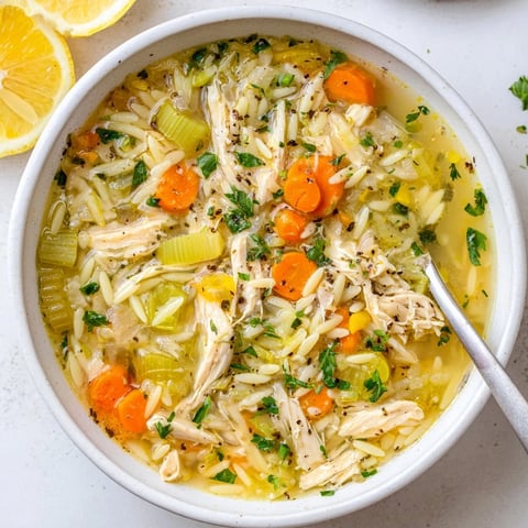 A steaming bowl of Lemon Pepper Chicken Orzo Soup, featuring tender shredded chicken and bright lemon wedges on the side.  