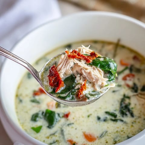 Close-up of Creamy Tuscan Chicken Soup in a rustic bowl, garnished with Parmesan and fresh herbs.