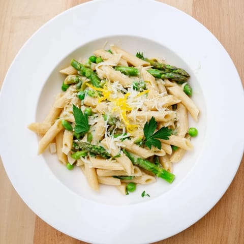 Bright green asparagus, peas, and green beans mingle with penne in a glossy garlic-Parmesan sauce, garnished with fresh basil for a vibrant spring meal.
