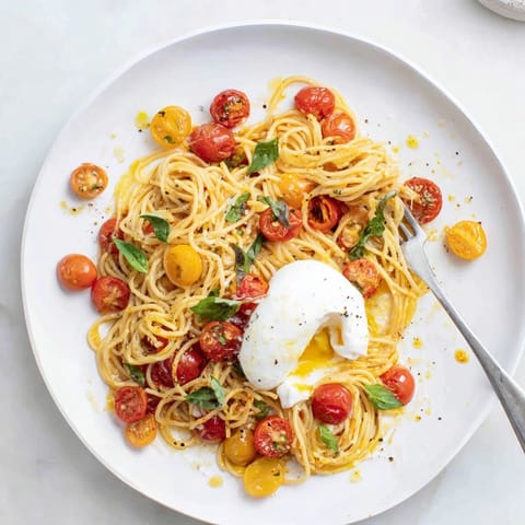 Close-up of Burrata Caprese Pasta showing a torn burrata ball melting into linguine with juicy tomatoes and basil leaves.
