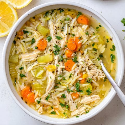 A steaming bowl of Lemon Pepper Chicken Orzo Soup, featuring tender shredded chicken and bright lemon wedges on the side.  