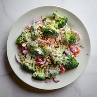 Vibrant green broccoli florets tossed in a creamy garlic Parmesan dressing, topped with toasted almonds for crunch, served in a white bowl.
