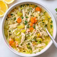 A steaming bowl of Lemon Pepper Chicken Orzo Soup, featuring tender shredded chicken and bright lemon wedges on the side.  