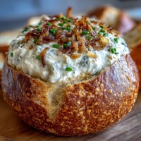 Creamy caramelized onion dip served in a warm sourdough bread bowl, garnished with fresh chives.  